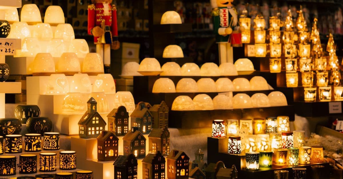 クリスマスマーケットの屋台に、温かな光を放つランプやろうそく形の照明、木製の小さな家が並んでいる。