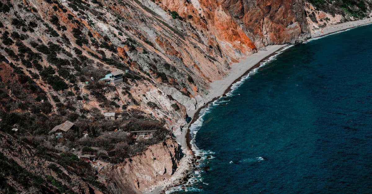 A narrow beach curves beneath rugged cliffs beside the deep blue sea on Albania’s coast.