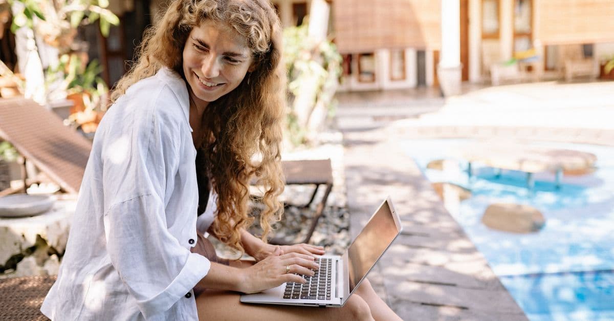 Mujer trabajando en laptop junto a la piscina, conectada con travel eSIM durante su working holiday