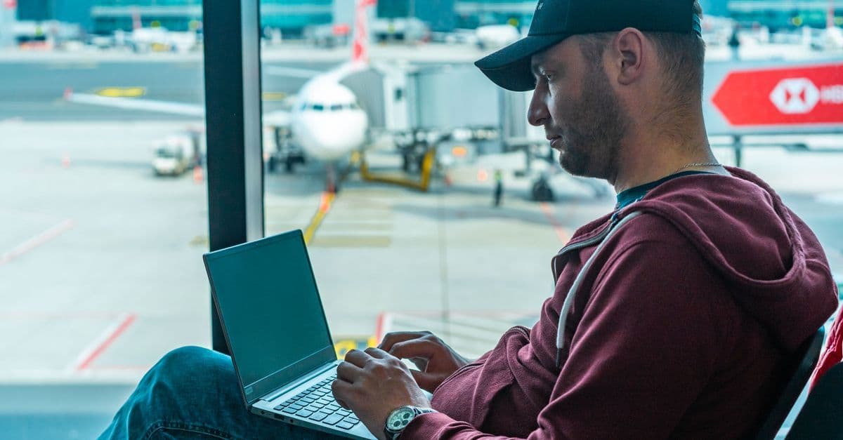Traveller working on a laptop at an airport gate to stay connected online during flight connections.