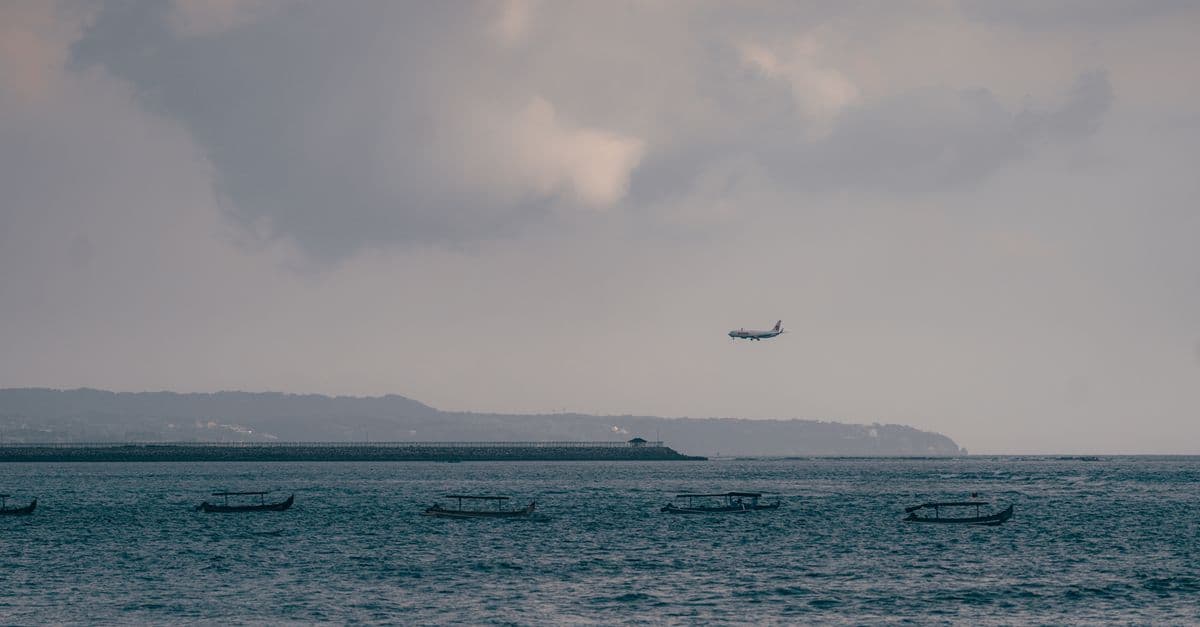A plane descends over the sea off Kuta, Bali, with traditional jukung outrigger boats bobbing below.